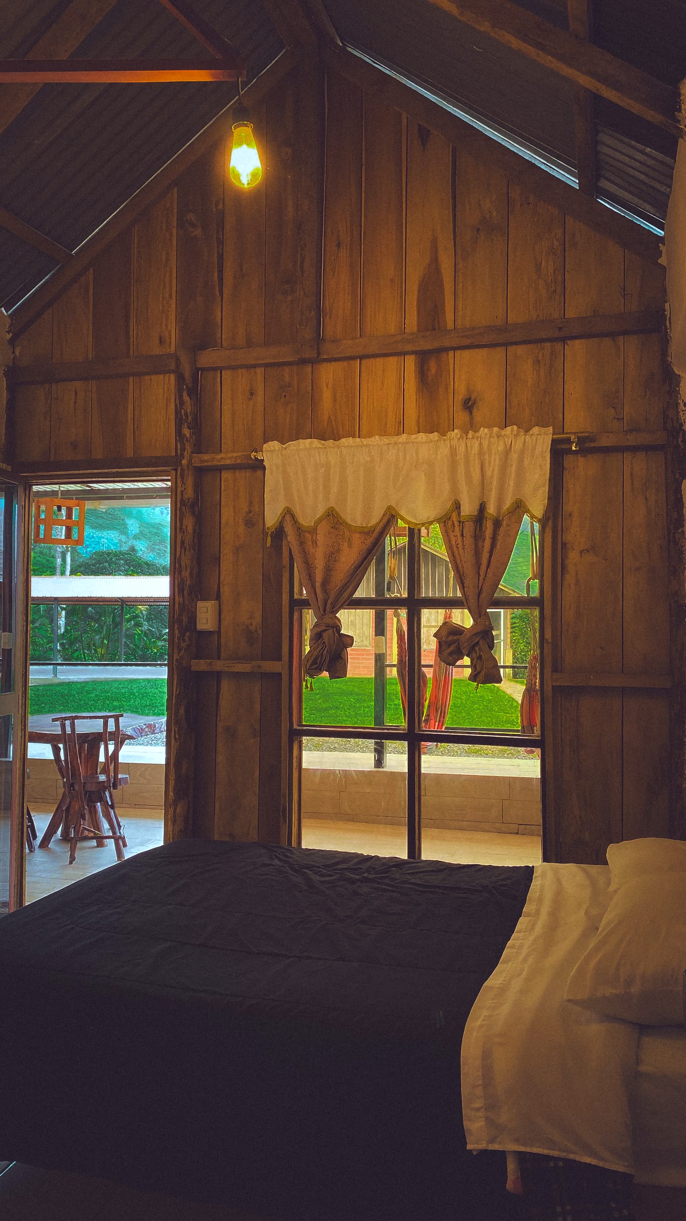 Interior cálido de la cabaña de madera: cama matrimonial junto al ventanal con vista al verde