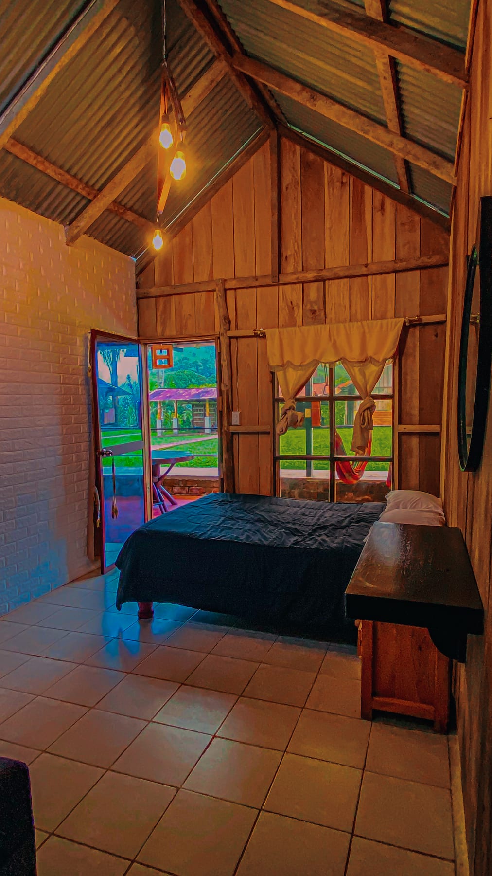 Interior de la cabaña rústica de madera con cama matrimonial y puerta al jardín